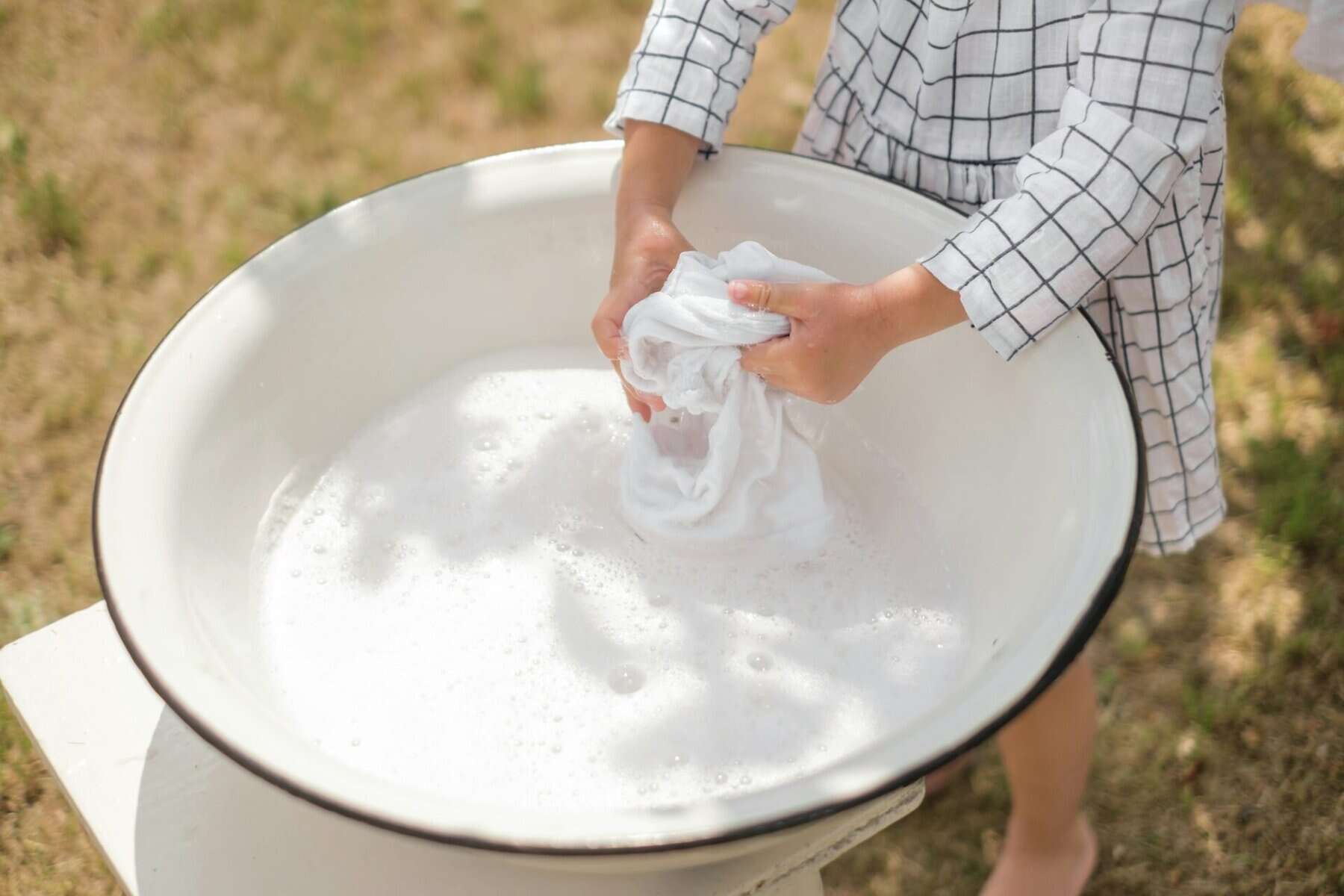 Hands washing a white vintage textile in a clean basin of distilled water