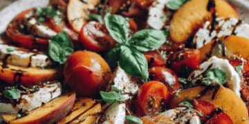 Peach caprese salad with torn mozzarella, basil, and balsamic glaze on a platter