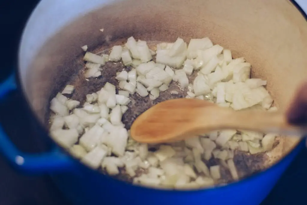 Southern Black Eyed Peas 8 Onions are sautéing in a blue iron pot, dutch oven, on a stovetop