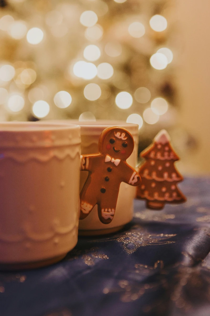Festive holiday cookies with gingerbread man and christmas tree decorations on a table, blurred christmas lights in the background, perfect for christmas celebration and baking themes.