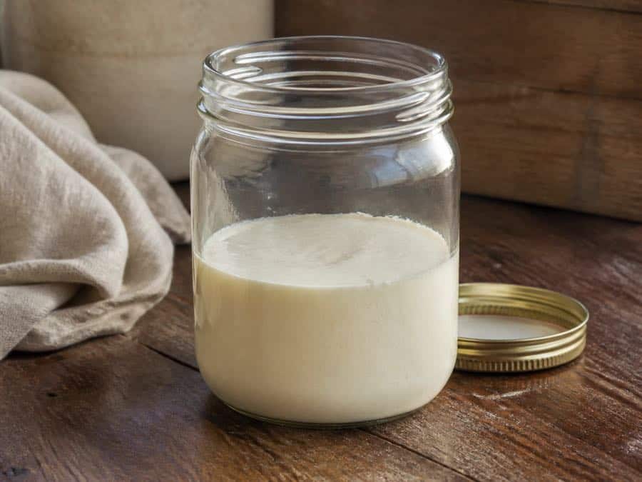 A clear jar filled halfway with raw milk cream, leaving enough room for churning.