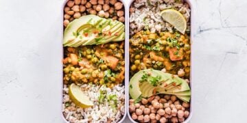 Two compartment bento box with chickpeas, rice, avocado, and lemon slices, perfect for a nutritious meal.