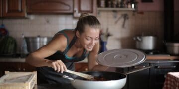 Healthy Home Cooking For A Balanced Lifestyle 7 Young woman cooking in a modern kitchen, smiling as she stirs a frying pan on the stove.
